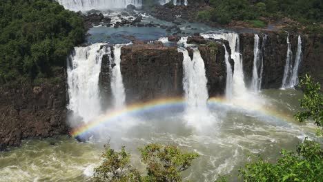 Beautiful-Rainbow-Colours-Formed-by-Waterfall-Splash-in-Iguacu-Falls,-Brazil,-High-Above-Angle-View-of-Beautiful-Cliff-Edge-and-Rough-Waterfalls-Looking-Over-Colourful-Bright-Rainbow-Arch