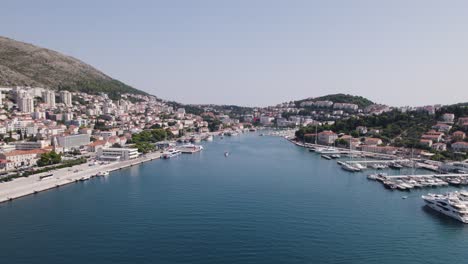 Puerto-De-Dubrovnik:-Yates,-Ciudad-Como-Telón-De-Fondo,-El-Resplandeciente-Abrazo-Del-Adriático---Aéreo