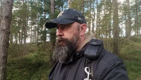 A-man-with-a-beard-wearing-a-baseball-cap-is-walking-quietly-along-a-sunny-path-in-the-woodland-of-Newborough,-Isle-of-Anglesey,-Wales
