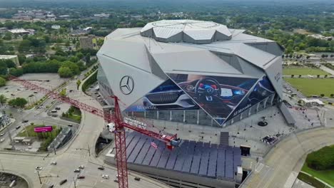 Toma-Aérea-De-Arriba-Hacia-Abajo-De-Una-Grúa-Con-Bandera-Estadounidense-Ondeando-Y-El-Estadio-Mercedes-Benz-En-Segundo-Plano.