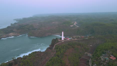 Aerial-orbiting-shot-of-lighthouse-at-Baron-beach-during-foggy-day,-Indonesia