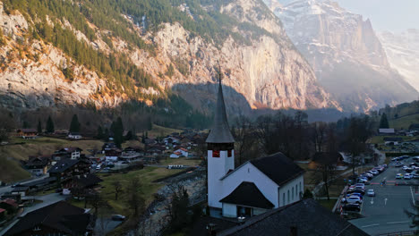Peaceful-church-by-the-river-in-Lauterbrunnen,-Switzerland-sits-in-the-shade-of-the-cliff-walls-above