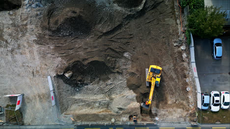 Static-aerial-bird's-eye-view-above-yellow-excavator-removing-dirt-from-construction-site