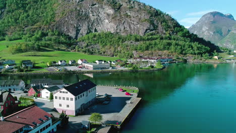 Aerial-panning-shot-of-the-small-municipality-of-Aurland-in-the-province-of-Vestland-in-Norway-with-historic-colorful-houses,-a-calm-river-and-the-landscape-with-mountains-in-the-background