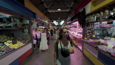 Foto-De-Dolly-Hacia-Atrás-De-Una-Mujer-Joven-Y-Bonita-Con-Una-Bebida-En-La-Mano-Mientras-Caminaba-Por-El-Mercado-Callejero-Cubierto-De-Málaga-En-España-Durante-Un-Viaje-De-Compras-De-Vacaciones-En-Cámara-Lenta.