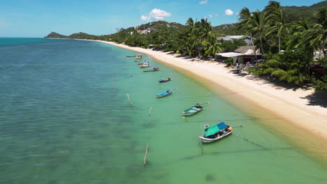 Sandy-Thailand-coastline-with-palms,-boats-and-small-village,-aerial-view