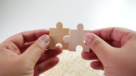 Jigsaw-Puzzle-pieces-on-the-table-then-the-lefthand-and-the-righthand-put-two-pieces-together-making-them-fit-before-laying-on-the-table
