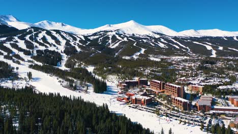 Beautiful-Aerial-Drone-View-of-Ski-Resort-with-People-Riding-Chairlifts-up-Slopes-and-Trails-on-top-of-Mountains-Covered-in-White-Powder-Snow