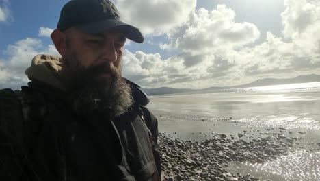 Adventurous-bearded-man-slow-motion-walking-windy-coastal-waterfront,-early-morning-exploring