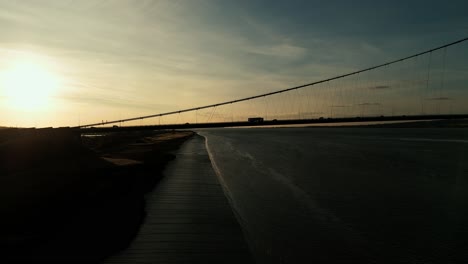 Humber-Bridge-bathed-in-sunset's-warmth,-cars-traverse-its-length