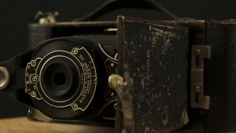 Dark-narrow-focus-antique-camera-revolves,-lens,-viewfinder,-bellows