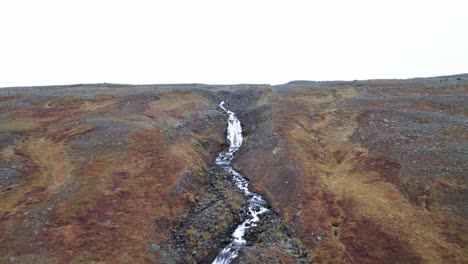 Aerial:-Distant-reveal-from-above-the-waterfall-to-the-bottom-of-Rjukandafoss,-a-hidden-treasure-amidst-Iceland's-pristine-wilderness