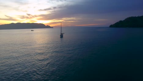 Drone-flying-low-over-the-Ballena-Bay-water-in-Costa-Rica-towards-a-few-sailing-yachts-anchored-in-the-calm-water-during-sunset