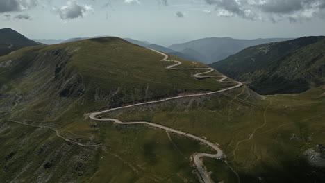 A-breathtaking-view-of-Transalpina's-serpentine-roads-in-Romania,-enveloped-by-verdant-mountainsides-and-punctuated-with-cloud-shadows