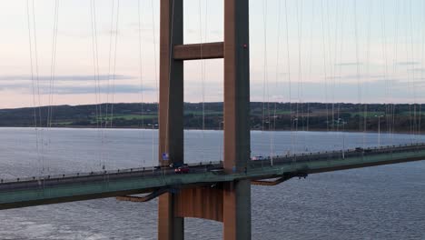Twilight's-embrace:-An-aerial-drone-unveils-the-Humber-Bridge's-splendor-at-sunset,-with-cars-creating-a-tranquil-tableau