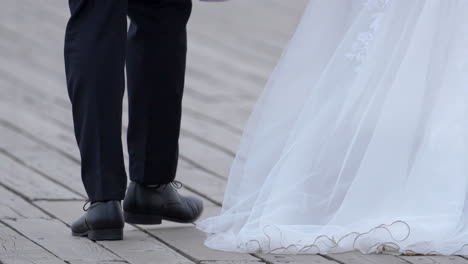Close-up-of-a-groom's-feet,-stepping-on-a-wooden-boardwalk,-trailing-bride's-dress
