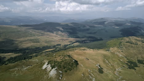 Breathtaking-aerial-view-of-Romania's-Transalpina,-showcasing-lush-meadows,-dense-coniferous-forests,-and-rugged-terrains-under-a-cloudy-sky,-emphasizing-nature's-grandeur