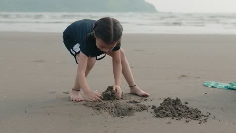 Ein-Junges-Mädchen-Verbringt-Einen-Lustigen-Tag-Am-Strand,-Spielt-Und-Schaufelt-Sand-Mit-Den-Händen