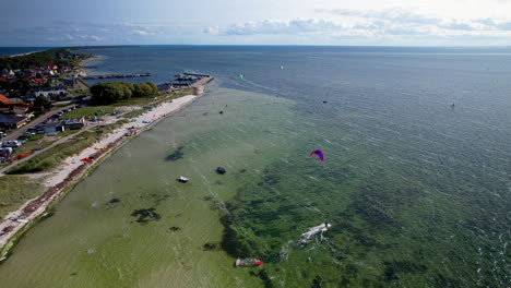 A-breathtaking-aerial-view-of-Kuźnica,-a-seaside-resort-in-Pomerania,-Poland,-featuring-a-parachute-surfer-gliding-over-the-emerald-waters-on-a-sunny-day