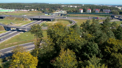 Luftaufnahmen-über-Den-Wäldern-Einer-Stark-Befahrenen-Autobahnkreuzung-In-Der-Nähe-Von-Wielki-Kack,-Gdynia,-Polen,-Bei-Sonnigem-Wetter-Und-Der-Ostsee-Am-Horizont