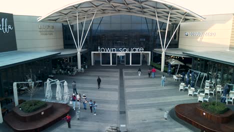 Toma-De-Drone-De-La-Entrada-De-La-Plaza-De-La-Ciudad-En-El-Centro-Comercial-De-África-Con-Gente-Caminando-En-Primer-Plano.