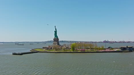 Eine-Umlaufende-Luftaufnahme,-Die-Eine-Livree-Statue-Auf-Der-Insel-Und-Einen-Fliegenden-Hubschrauber-Im-Hintergrund-Vor-Blauem-Himmel-Zeigt-–-New-York-City,-USA
