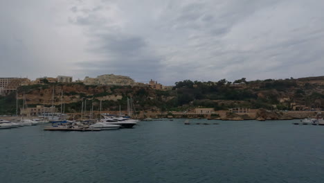 Vista-Aérea-De-Un-Hermoso-Puerto-En-El-Mar-Azul-En-La-Costa-De-Malta-En-La-Valeta,-Con-Vistas-A-Veleros,-Barcos-Y-Edificios-Históricos-Al-Fondo-Durante-Un-Viaje-De-Vacaciones-De-Verano
