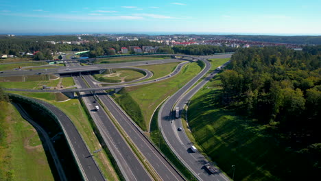 Aerial-view-of-a-sprawling-highway-interchange-with-multiple-lanes-and-overpasses,-surrounded-by-trees-and-cityscape