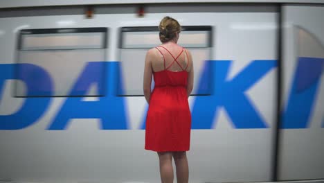 Hübsche-Frau-In-Einem-Roten-Kleid,-Die-Darauf-Wartet,-Mit-Dem-BTS-Sky-Train-In-Bangkok,-Thailand,-Zu-Fahren