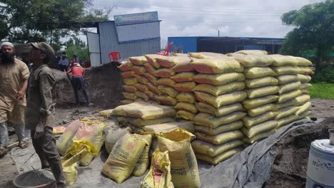 A-team-of-male-laborers-in-dusty-conditions-move-heavy-bags-of-cement-at-a-building-construction-site-in-India