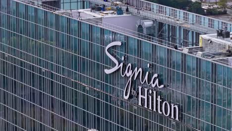 Zoom-drone-shot-showing-sign-of-Signia-by-Hilton-Hotel-on-mirrored-building-in-Atlanta-during-sunny-day---panning-shot