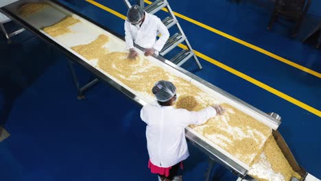 Aerial-camera-pans,-peanut-butter-being-checked-by-women-wearing-safety-gloves-on-a-conveyor-belt-in-a-peanut-butter-factory