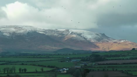 Comeragh-Mountains-Waterford-Ireland-winter-farmland-under-snow-covered-mountains-establishing-shot