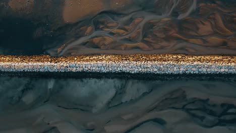 Descending-top-down-shot-of-rocky-breakwater-in-Provincetown-at-sunset-time---Pattern-of-water-on-the-ground