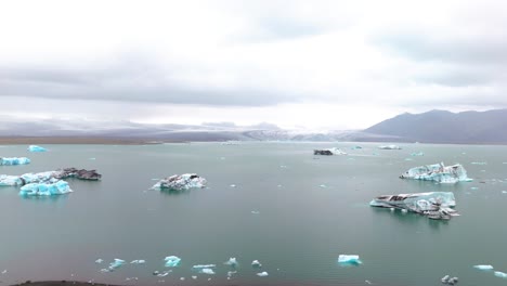 Luftaufnahme-Eines-Gletschersees-Im-Norden-Islands-Mit-Eisbergen-Und-Umgeben-Von-Bergen