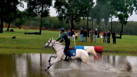 A-rider-at-full-gallop-through-a-water-pool-during-a-cross-country-horse-race
