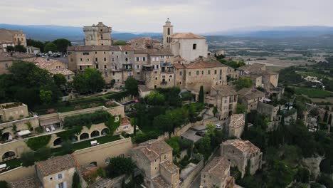 Aerial-view-showing-historic-city-of-Gordes-in-France-located-on-hill-with-scenic-landscape-in-background