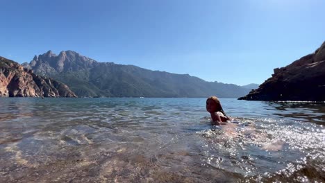 Young-little-girl-enjoy-bathing-and-swimming-in-crystal-clear-sea-water-of-Bussaglia-beach-in-Corsica-island,-France