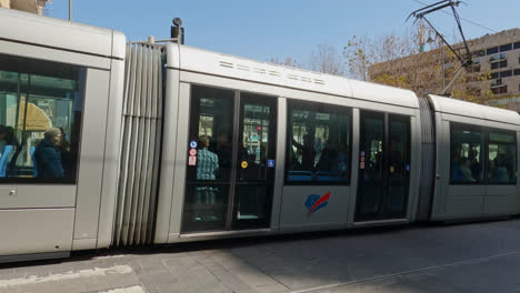 Pan-follows-light-rail-tram-moving-across-city-on-tracks-in-shadows-of-buildings