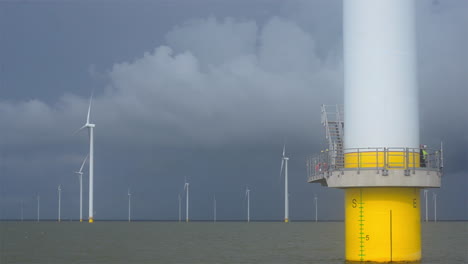 Wind-turbine-with-maintenance-crew-at-an-off-shore-wind-park,-filmed-from-an-inspection-vessel
