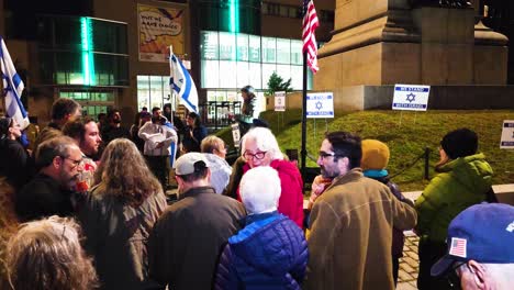 Detrás-De-Un-Grupo-De-Hombres-Y-Mujeres-Que-Se-Han-Reunido-En-Una-Plaza-Pública-En-Portland-Maine-Para-Apoyar-Al-Estado-De-Israel.