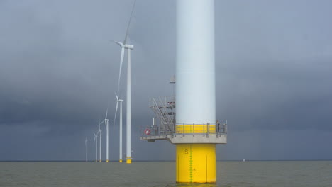 Sailing-near-a-row-of-turbines-at-a-near-shore-wind-park,-REVEALING-shot-with-PERSPECTIVE
