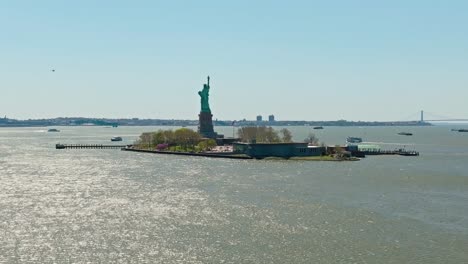 Aerial-wide-shot-showing-Statue-of-Liberty-on-island-during-sunny-day-in-New-York-City