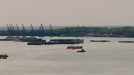 Descending-drone-revealing-the-two-ferries-passing-by-and-the-industrial-backdrop-with-tall-cranes-and-sturdy-stationary-barges-across-the-water