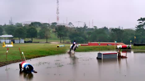 Foto-Panorámica-De-Un-Jinete-Con-Su-Caballo-Viniendo-Del-Prado-Al-Agua-Para-Saltar-Un-Obstáculo