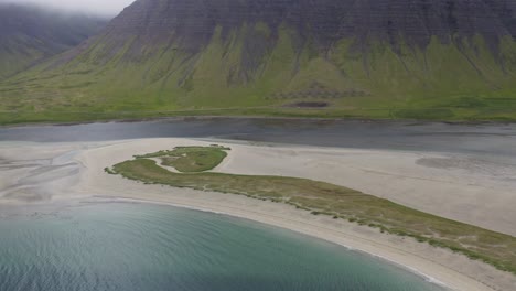 Aerial-approaching-shot-of-white-sandy-reef-on-Iceland-Island-with-green-hills-in-background-during-cloudy-day---tilt-down-movement