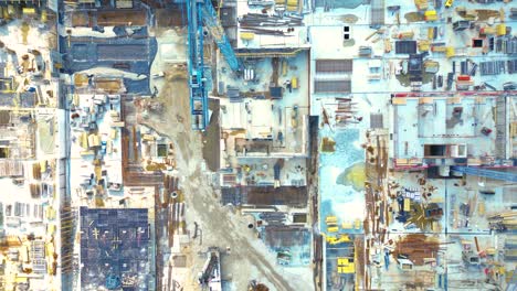 Aerial-Bird-Eye-View-Of-a-Construction-Site-Building-Cranes-Looking-Down-Industrial-Machinery-Area-around-Residential-Urban-Apartments