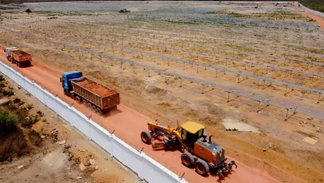 static-shot-of-trucks-and-heavy-machinery-for-road-construction-passing-by-at-solar-power-plant-project-in-Gambia,-West-Africa