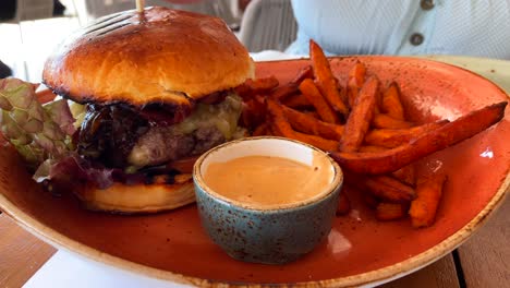 Dipping-sweet-potato-fries-in-spicy-mayonnaise-sauce,-cheeseburger-with-a-brioche-bun,-fast-food-restaurant,-4K-shot
