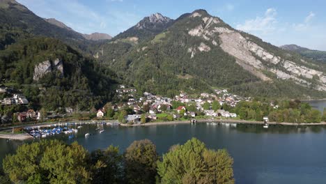 Eine-Luftaufnahme-Von-Walensee-Zeigt-Einen-Kleinen-Yachthafen-Und-Wohnhäuser-Mit-Den-Majestätischen-Grünen-Schweizer-Alpen-Im-Hintergrund-An-Einem-Sonnigen-Tag